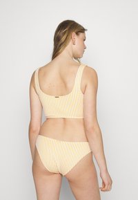 Biquíni riscado em amarelo e branco; apresenta um topo com costas em forma de scoop e fundos de cintura baixa combinando, feitos de um tecido liso e elástico.