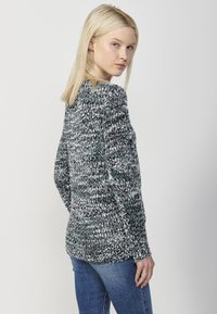 Pulover tricotat în negru, verde și alb. Prezintă o croială lejeră, guler rotund și mâneci lungi cu un model texturat.