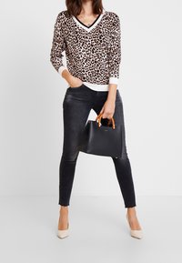 Pull à imprimé léopard avec bordure blanche, jean skinny foncé, talons beiges et sac à main noir avec anses marron. Accent sur une tenue décontractée contemporaine.