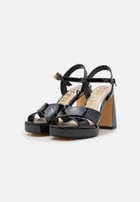 Zwarte lakleren sandalen met hoge hakken en een platform, voorzien van kruislings strappy en een enkelbandje met een gouden gesp accent.