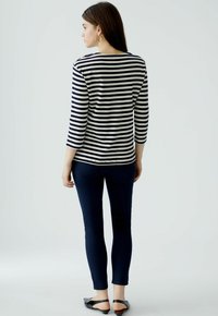 Zwart-wit gestreepte langemouwshirt, gecombineerd met donkerblauwe strakke broek en zwarte platte schoenen. Het model staat met de rug naar de camera gekeerd.