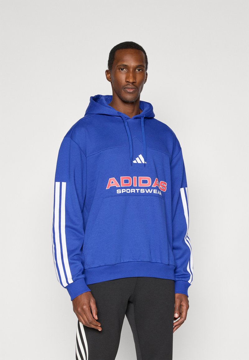 Modra kapuca s puloverjem z belimi črtami na rokavih in velikim rdečim napisom "ADIDAS SPORTSWEAR" na sprednji strani, pletenina.