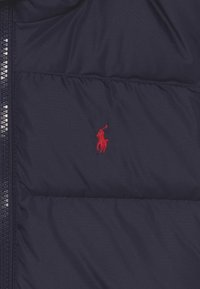 Tmavě modrá prošívaná péřová bunda s prošívanou texturou, s červeně vyšívaným logem polo na hrudi a zapínáním na zip vpředu.