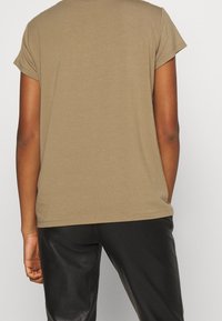 T-shirt à manches courtes en khaki en coton lisse, avec un col rond classique et une coupe décontractée. Pantalons slim noirs visibles en dessous.
