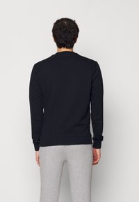 Zwarte sweatshirt met lange mouwen, ribgebreide manchetten en zoom. Gemaakt van katoen, standaard ronde halslijn, gezien vanuit de achterkant.