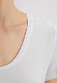 Biały t-shirt z krótkim rękawem, o okrągłym dekolcie, wykonany z miękkiego, lekkiego materiału. Posiada lekko melanżową teksturę.