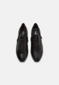 Chaussures en cuir noir à lacets avec des fermetures éclair sur les côtés, vues de dessus sur un fond blanc uni.