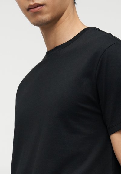 T-shirt noir à manches courtes en tissu doux, doté d'un col rond et d'une texture lisse, porté sur le haut du torse d'une personne.