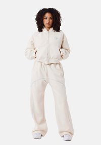 Crème kleurige hoodie en joggingbroek set, gemaakt van zachte stof, met een ritssluiting, ribgebreide manchetten en contrasterende blauwe stiksels.