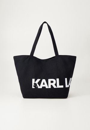 Czarna torba typu tote z długimi uchwytami i białym, częściowym nadrukiem "KARL LA" z przodu na jednolitym tle.