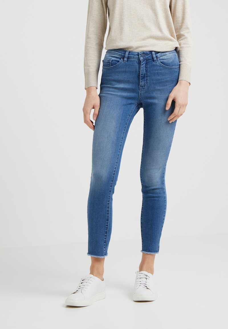 Trånga jeans i medelblå denim, med en blekt tvätt, medelhög midja och rå nederkant. Förenas med vita sneakers och en beige topp.