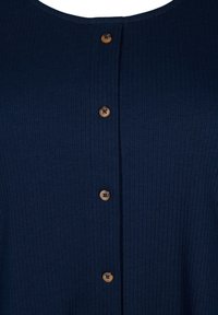 Top ribbed blu navy con scollatura tonda e sei bottoni arrotondati marroni lungo la parte frontale. Il tessuto ha un aspetto strutturato.