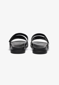 Svarte sandaler med to brede stropper, flat såle og jevn tekstur. Minimalistisk design som viser en enkel og praktisk stil.