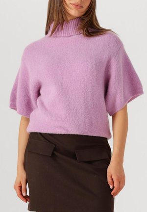 Kortoe sug sweater in lavendel met hoge ribgebreide halslijn en een zachte, pluizige textuur, gedragen over een donkerbruine rok met klepzakken.