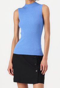 Sleeveless ribbed blue top paired with a black buttoned asymmetrical mini skirt worn by a standing person.
