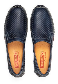 Marineblaue Leder-Slipper mit perforiertem Design, genähten Details und braunen Innensohlen. Abgerundete Zehen und elastische Seitenpaneele für eine bequeme Passform.