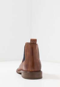 Bottine Chelsea en cuir marron avec panneaux latéraux élastiques et talon empilé. Présente un logo au talon et une texture lisse.