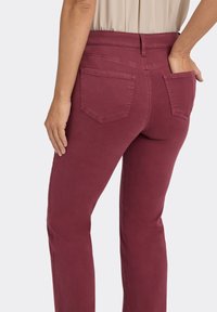 Bordeauxrode spijkerbroek met een getailleerde taille, twee achterzakken en een licht taps toelopende pijp. Soepele textuur en katoenmix materiaal.