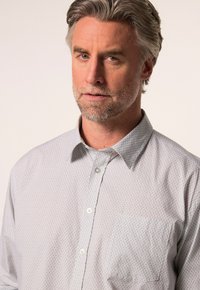 Camicia grigia chiaro con bottoni, caratterizzata da un sottile motivo geometrico, colletto a punta e una tasca sul petto. Tessuto morbido.