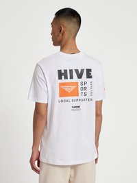 Vit bomullst-shirt med en djärv grafisk design på baksidan med svart och orange text och logotyper. Kort ärm och rund halsringning.