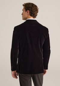 Juodas aksominis švarkas, prigludusio dizaino, su viena skeltuke gale, su užsegamomis rankogaliais ir elegantiška siluetu. Be matomų raštų ar akcentų.