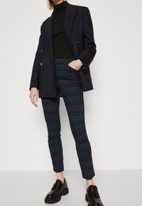 Marinblå dubbelknäppt kavaj, svart turtleneck, grön och marinblå rutiga byxor. Svarta kraftiga loafers med pälsdetaljer.