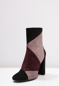Kotníkové boty v černé, bordó a šedé suede s špičatou špičkou a vysokým blokovým podpatkem. Má geometrický design s barevnými bloky.