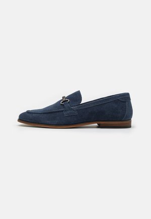 Navy suede loafer with a rounded toe, small decorative accent, and a contrasting brown sole. Smooth texture with subtle stitching details.