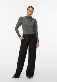 Metallic pilkos spalvos ilgomis rankovėmis viršus su drapiruotu kaklu, derinamas su juodomis plačiomis kelnėmis aukštu liemeniu ir juodais bateliais su baltais akcentais.