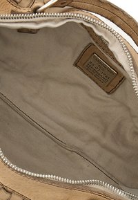 Interno di una borsa in pelle color cuoio con fodera in tessuto strutturato, dotato di un'etichetta del marchio visibile e di una cerniera argentata.