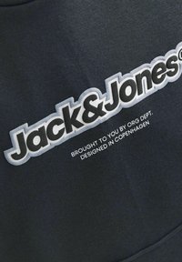 Svart tygtröja med stora, djärva, vita "Jack & Jones"-logotyp och grå detaljer, samt mindre text nedanför.