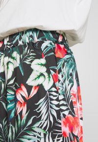 Bloemenbroek met een zwarte achtergrond en levendige roodgroene bladmotieven, een elastische tailleband en zijzakken.