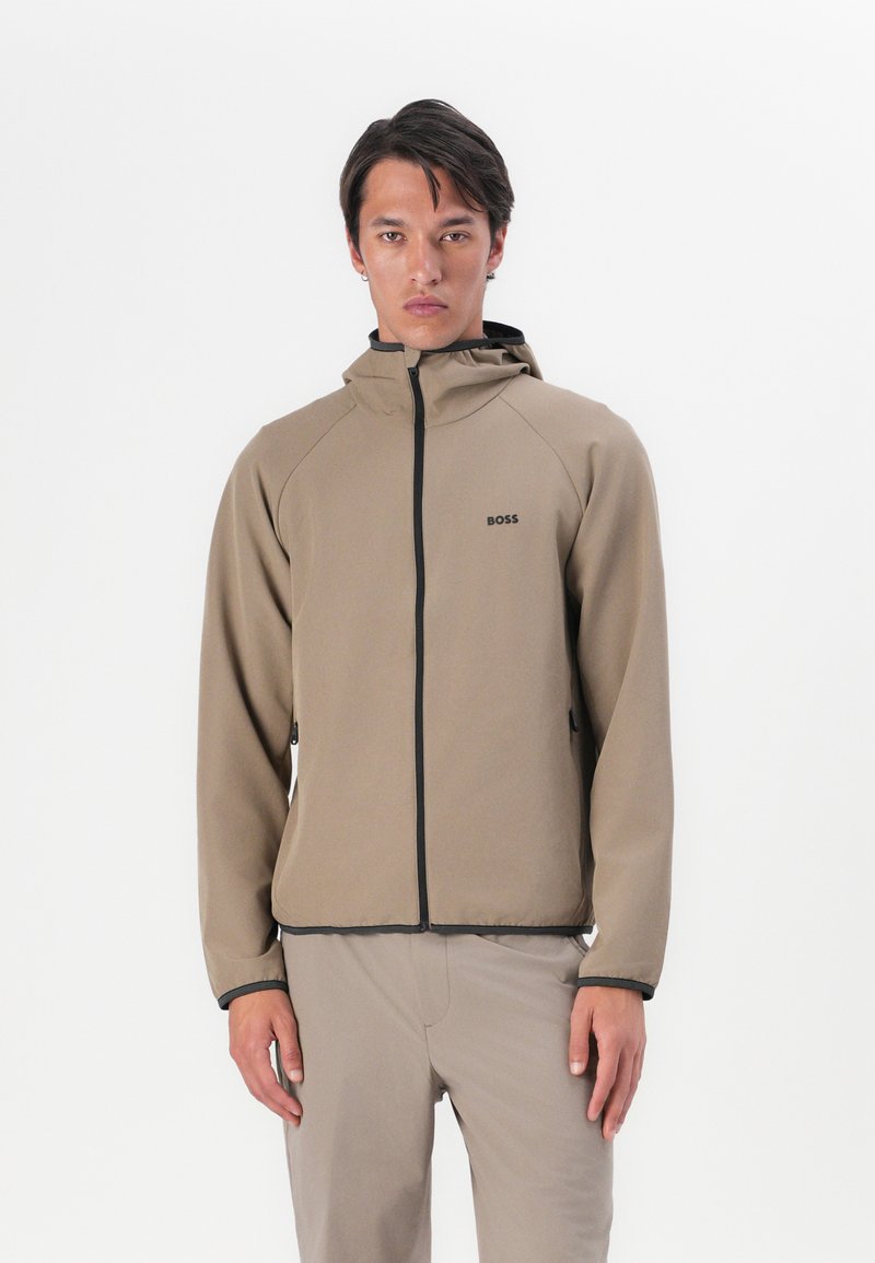 Lichtbruine hoodie-jack met zwarte ritsen en logo, met een rits aan de voorkant, lange mouwen en een gestroomlijnd ontwerp.