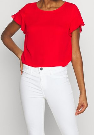 Top corto rosso a maniche corte con dettagli a volant, scollatura rotonda, realizzato in tessuto leggero. Abbinato a jeans bianchi skinny.