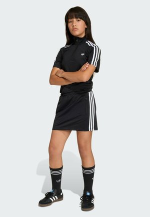 Čierny športový outfit s zipsom na vrchu a sukňou, s bielymi pruhmi. Doplnené čiernymi ponožkami a čiernymi topánkami s bielymi akcentmi.