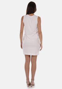 Vestito bianco senza maniche con una texture liscia, orlo lungo fino al ginocchio e design semplice. Il modello indossa scarpe con tacchi alti in tono neutro.