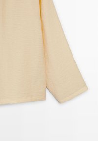 Crèmekleurige top met lange mouwen van zacht materiaal, met een ontspannen pasvorm, een licht asymmetrische zoom en zichtbare stiksel details.