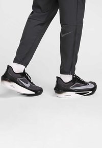 Mustat ja harmaat urheilukengät, joissa on hengittävä verkkopäällinen, paksu valkoinen välipohja ja kuvioitu ulkopohja parempaa pitoa varten.