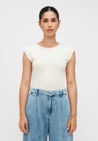 Witte geribbelde top met korte mouwen, gecombineerd met lichtblauwe high-waisted spijkerbroek. De top heeft een ronde halslijn en een aansluitend ontwerp.