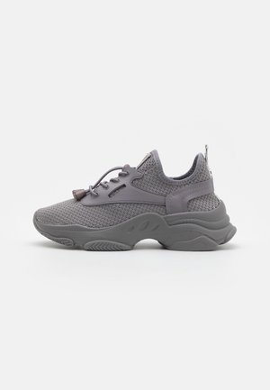 Grå mesh atletiksko med tykk bølget sål, slip-on design, justerbare snøretøjsøjer og en træksnøre på hælen.