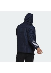 Námořnicky modrá péřová bunda s kapucí, s horizontálním prošíváním a třemi bílými pruhy na levém rukávu. Lehký materiál.