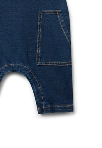 Le salopette in denim scuro presentano una grande tasca laterale, cuciture a contrasto e aperture delle gambe arrotondate, mettendo in evidenza una finitura del tessuto testurizzata.