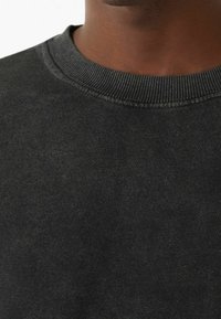 Czarny sweatshirt z okrągłym dekoltem i prążkowanym wykończeniem. Materiał wydaje się miękki i teksturowany, z lekko przygaszonym wykończeniem. Brak widocznych wzorów lub akcentów.