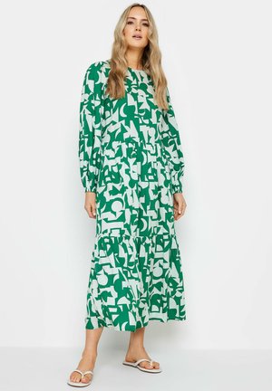 Lange groene jurk met witte abstracte patronen, met lange mouwen, een gelaagde rok en een elastische taille. Draag met witte sandalen.