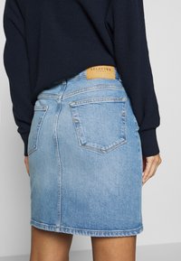 Hellblauer Jeansrock mit geradem Schnitt, Gesäßtaschen und einem hellbraunen Lederlabel am Bund. Strukturiertes Material mit einem verwaschenen Finish.