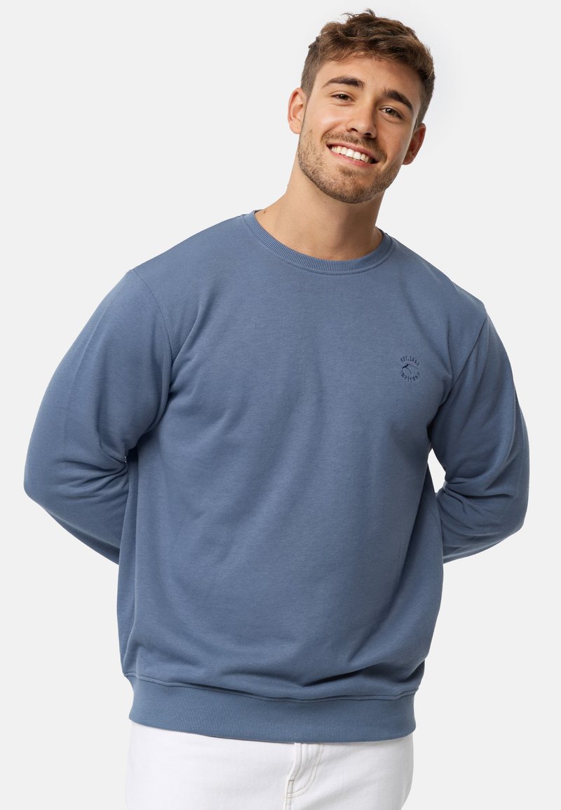 Sudadera de cuello redondo azul hecha de una suave mezcla de algodón, con mangas largas, puños acanalados y un pequeño logotipo en el pecho.