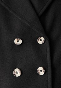Abrigo negro de doble botonadura con una textura suave, que presenta cuatro botones redondos contrastantes con un diseño moteado en la parte frontal.