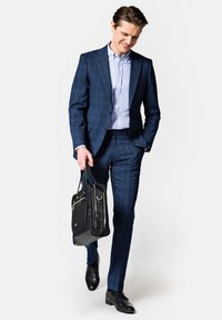 Granatowy garnitur w kratę o dopasowanym kroju, w połączeniu z jasnoniebieską koszulą. Model trzyma czarną torbę z srebrnymi akcentami, nosząc czarne buty wizytowe.