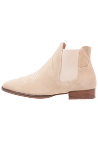 Botín de ante beige hasta el tobillo con paneles laterales elásticos, puntera afilada y tacón bajo de madera. Presenta costuras blancas discretas en la parte delantera.