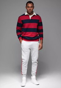Gestreiftes Rugbyshirt in Rot und Marineblau mit einem weißen Kragen, kombiniert mit grauen Jogginghosen mit roten Seitenstreifen, getragen mit weißen Sneakern.
